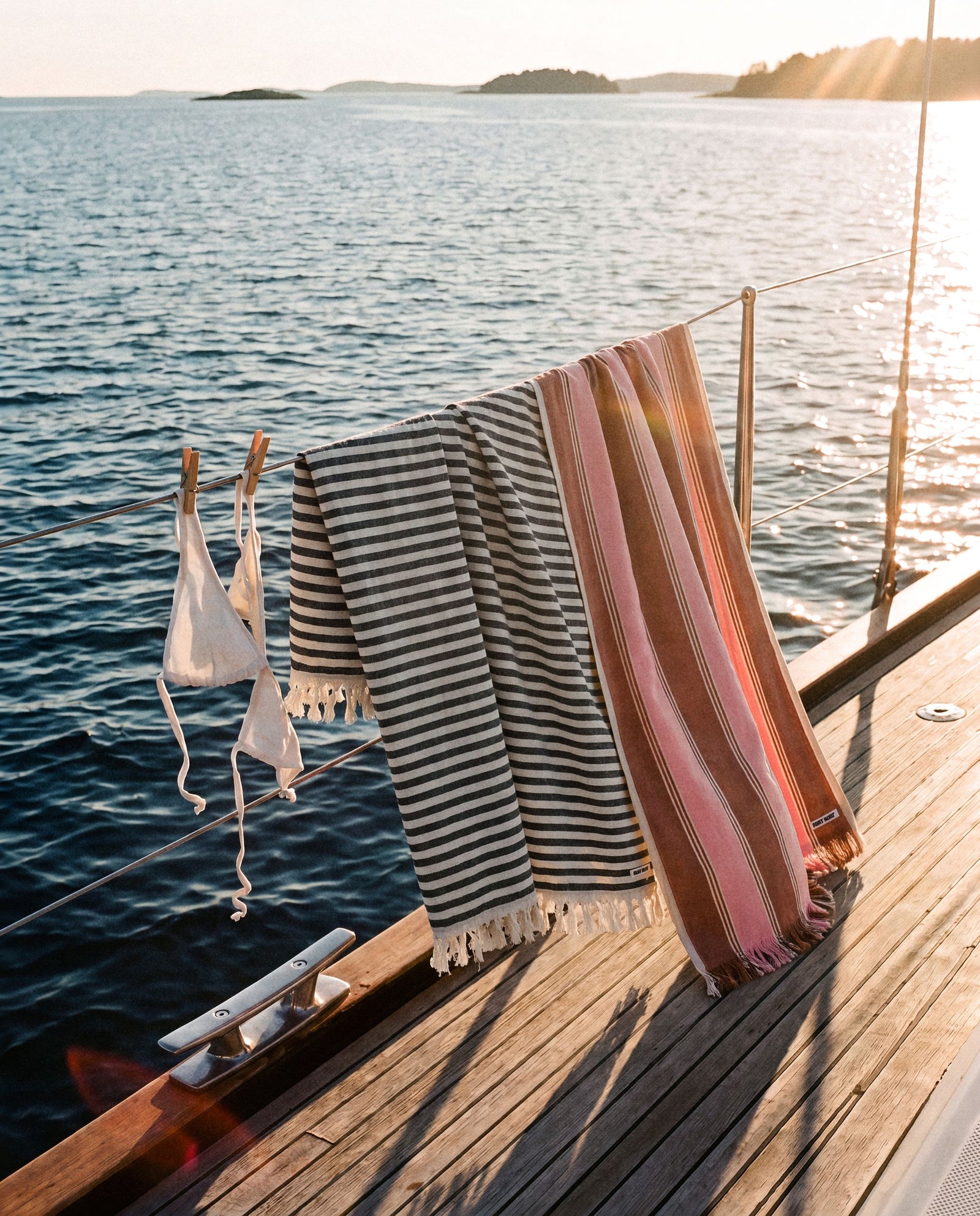 Striped Ruby Mint towels pegged along a boat rail at golden hour