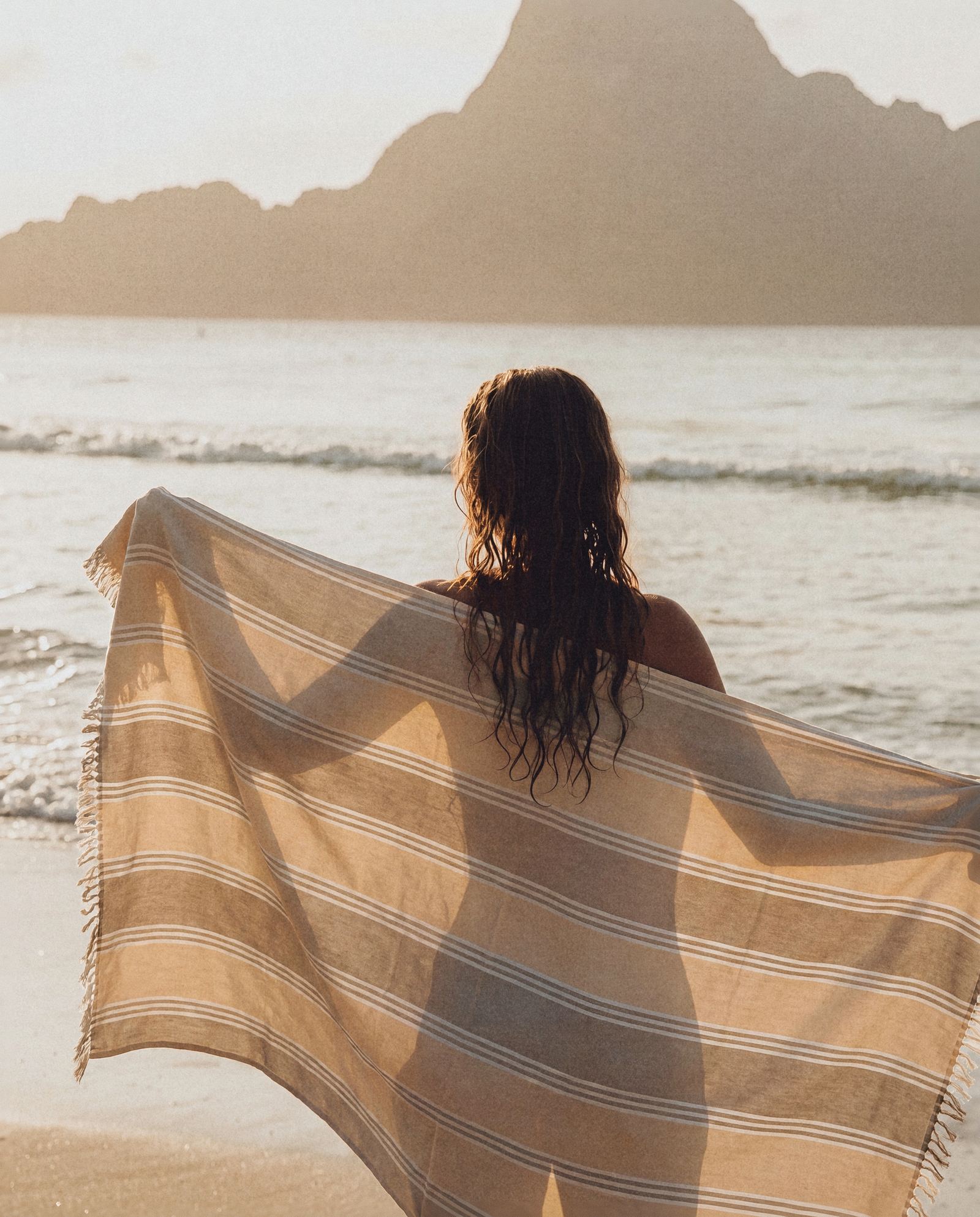 Model holding a striped Turkish towel open in the wind at the shoreline