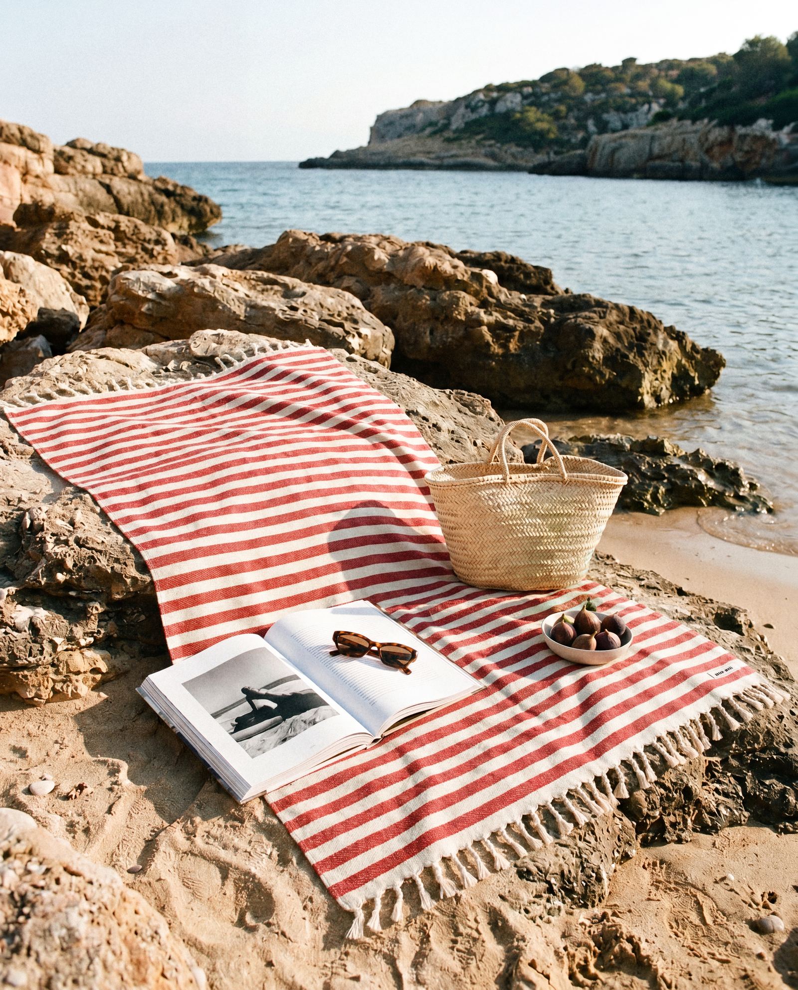 Red-striped beach towel laid over coastal rocks with a woven basket