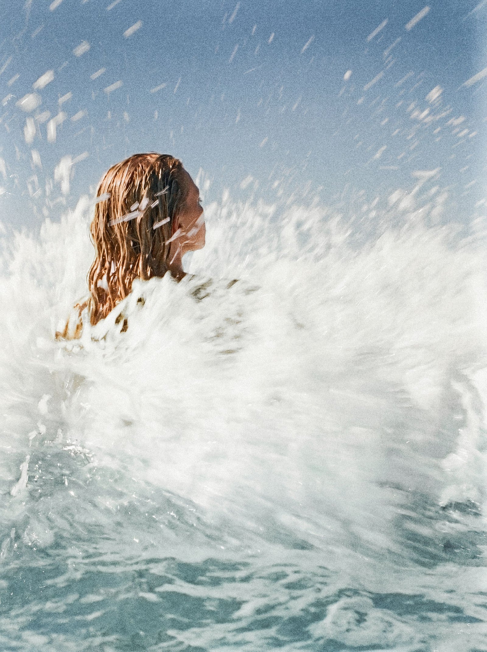 Swimmer surfacing through white water in bright sun