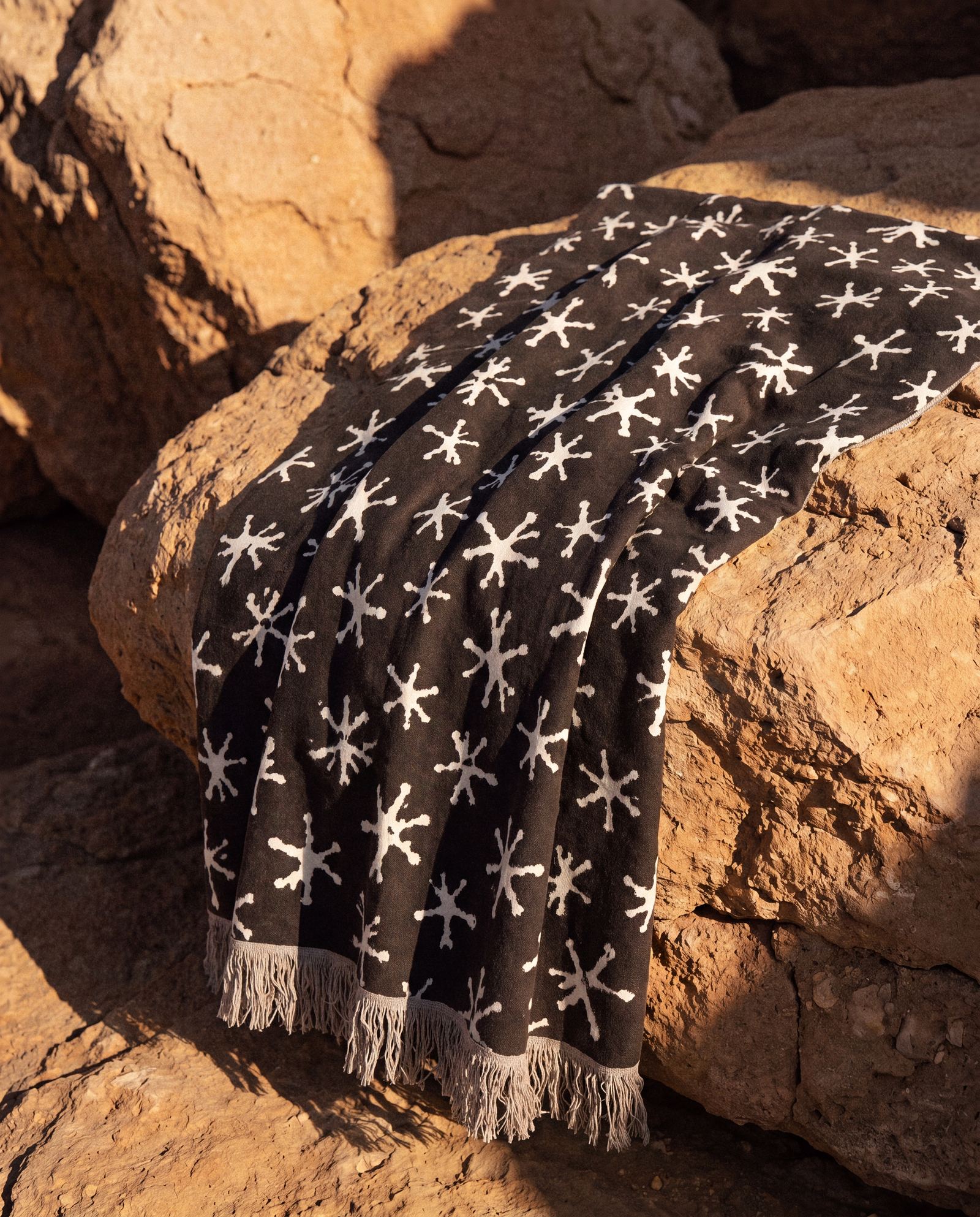 Starfish-print towel spread across sunlit coastal rocks